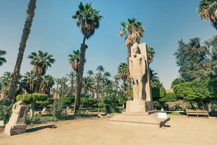 Standing statue of Ramses II on the background green palm trees in open air museum of Memphis, Egypt